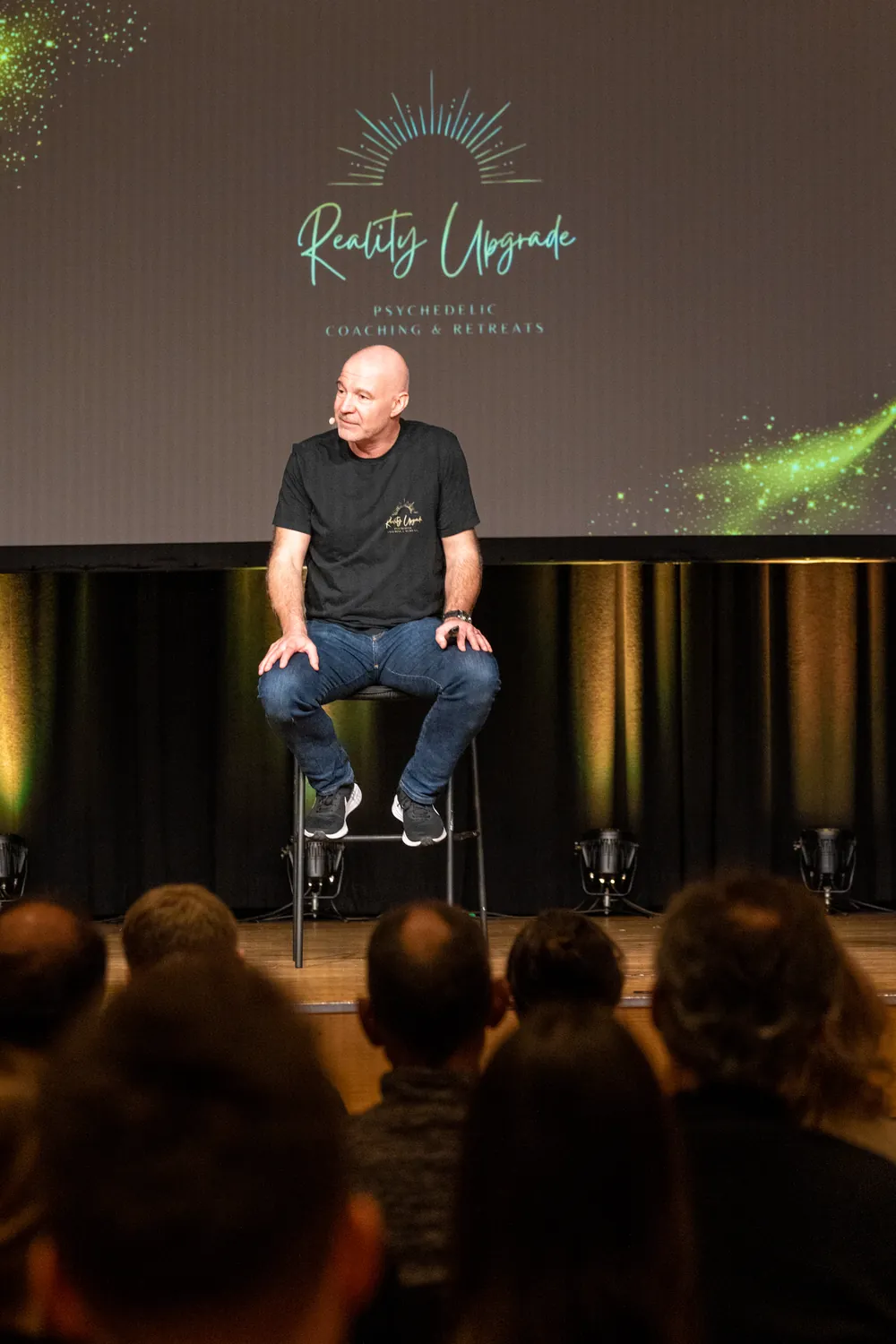 Dr. Stefan Frädrich sitzt auf einer Bühne vor einer Leinwand mit dem Reality-Upgrade-Logo, davor Publikum