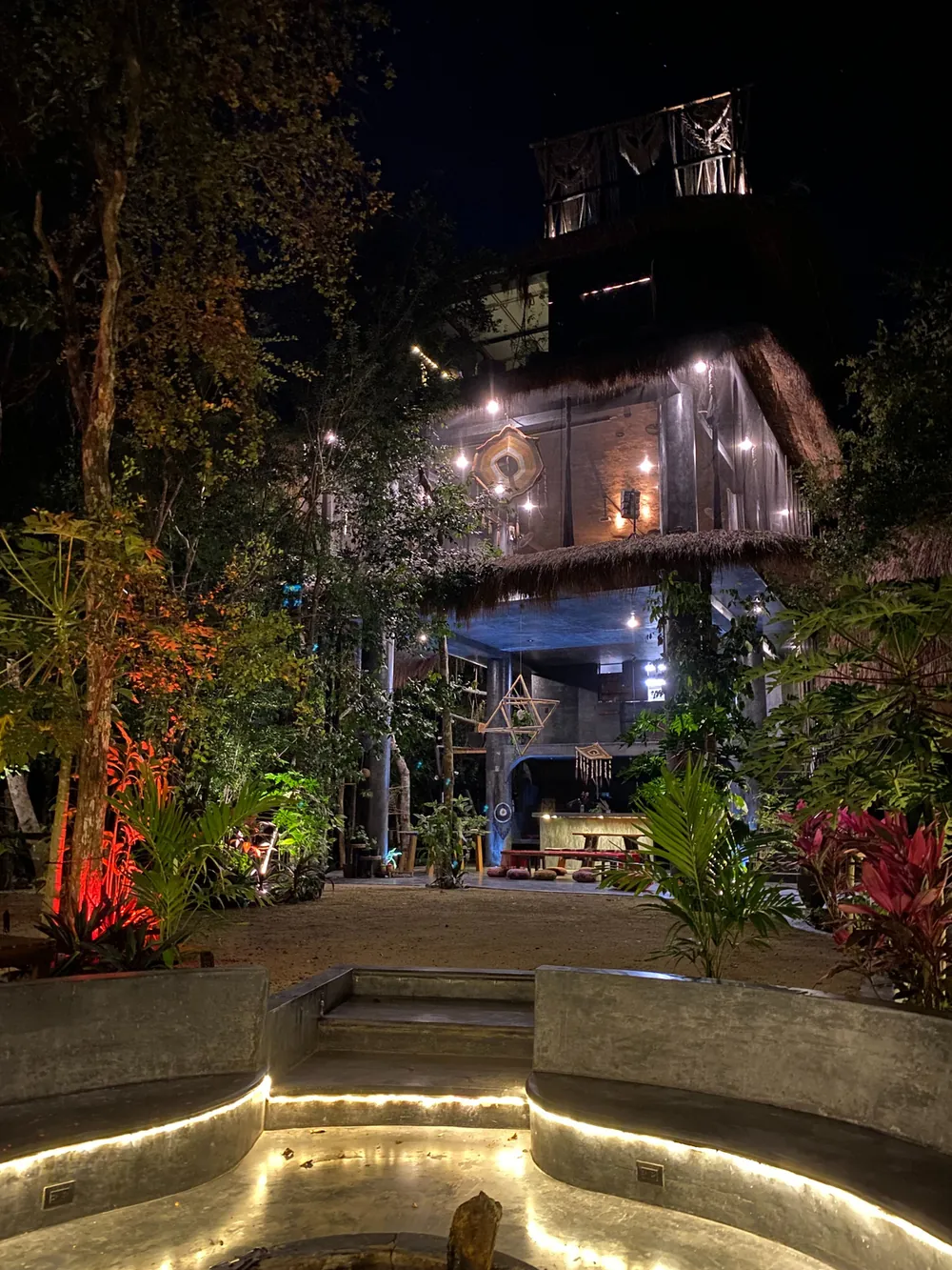 Beleuchteter runder Pool vor einem Haus im Dschungel bei Nacht