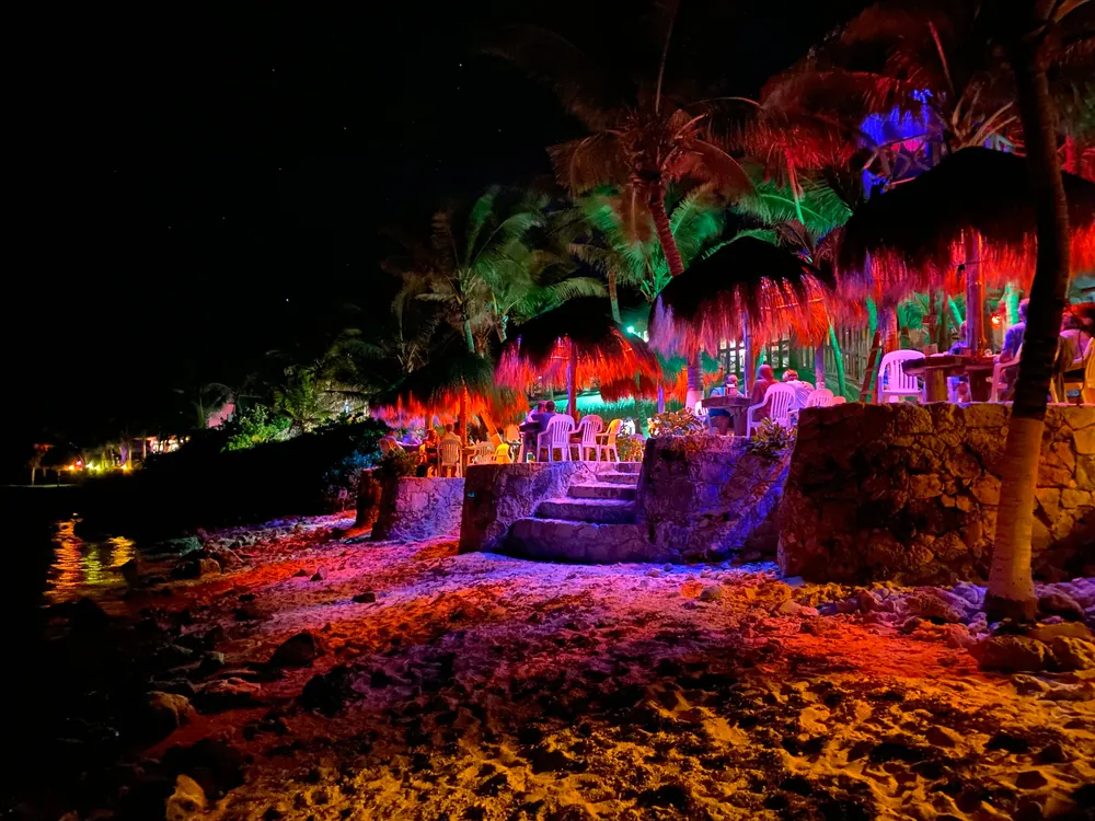 Strand bei Nacht mit Palmen und Strohschirmen in buntem Licht