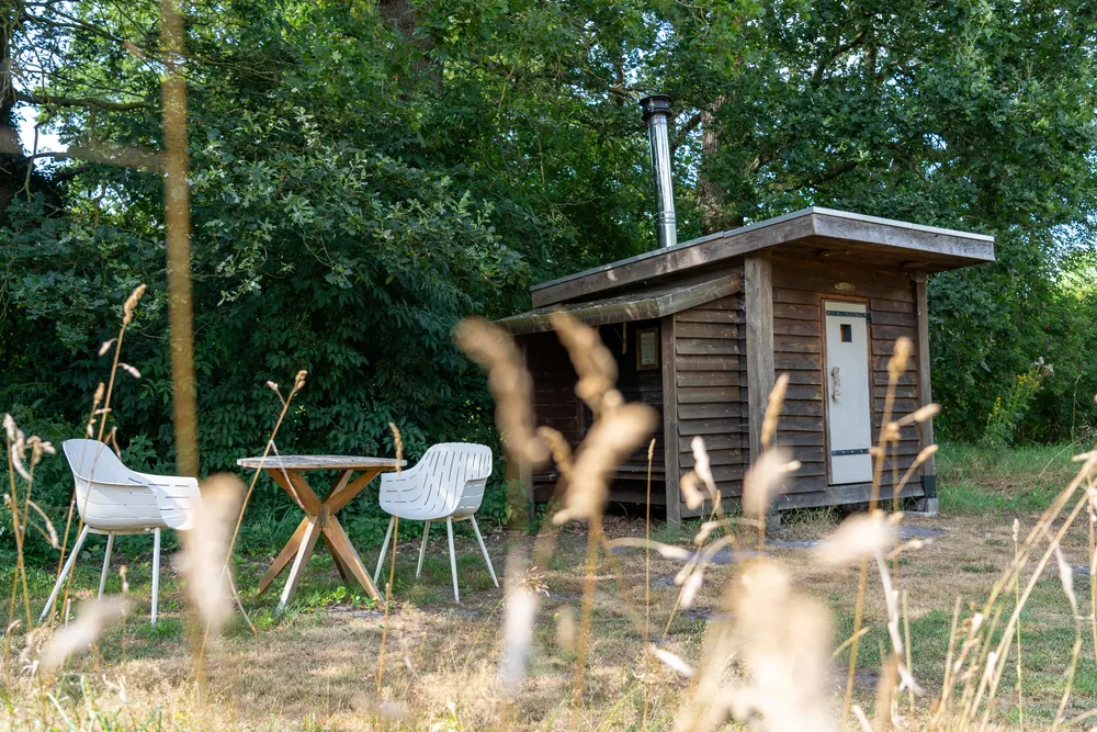 Holzhütte mit Schornstein, davor weiße Gartenstühle im Gras