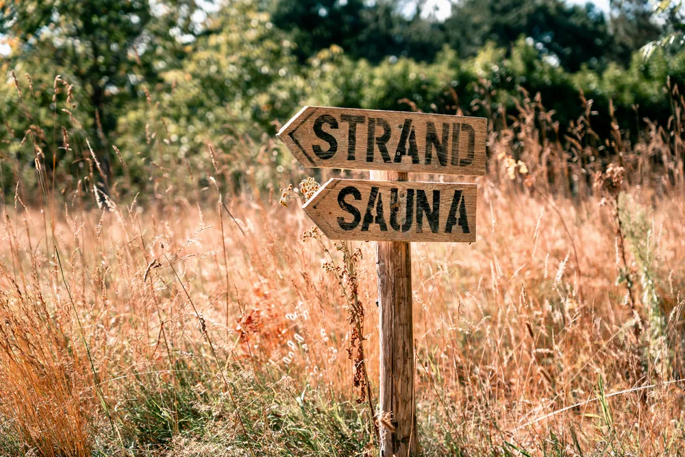 Hölzerner Wegweiser mit den Schildern Strand und Sauna im hohen Gras