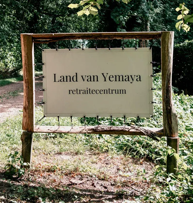 Schild mit der Aufschrift „Land van Yemaya retraitecentrum“ in einem Holzrahmen am Waldweg